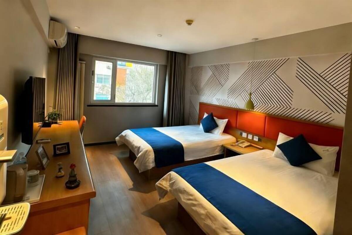 A hotel room with two beds, a desk, a chair, a TV, and a window.