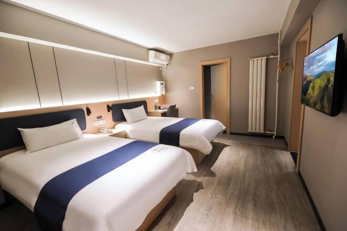 A hotel room with two beds, a desk, a chair, a TV, and a painting on the wall.
