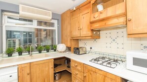 A kitchen with wooden cabinets, a gas stove, a toaster, and a microwave. - PML Apartments Victoria (London)