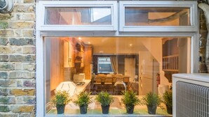 A kitchen with a dining area visible through a large window. - PML Apartments Victoria (London)