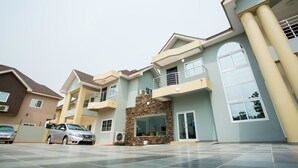 A modern multi-story residential building with a spacious driveway, a stone accent wall, and a large window. - Relle Suites Hotel (Accra)