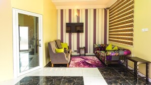 A living room with a sofa, armchair, and a flat-screen TV mounted on the wall. - Relle Suites Hotel (Accra)