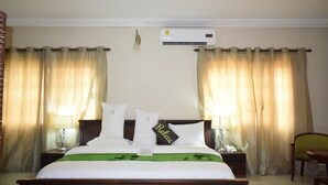 A hotel room with a bed, two nightstands, a chair, and curtains. - Relle Suites Hotel (Accra)