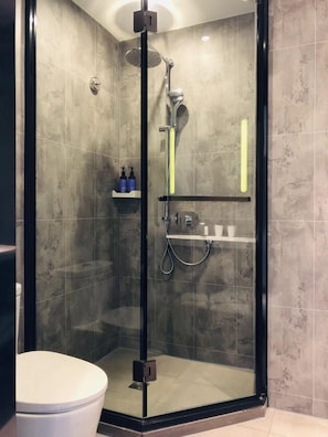 A modern bathroom with a glass-enclosed shower, a toilet, and a shelf with toiletries.