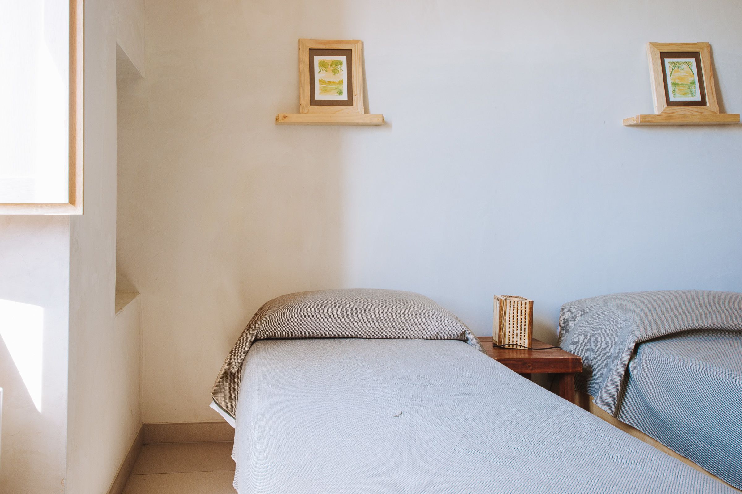 Una habitación con dos camas, una mesita y dos cuadros en la pared.