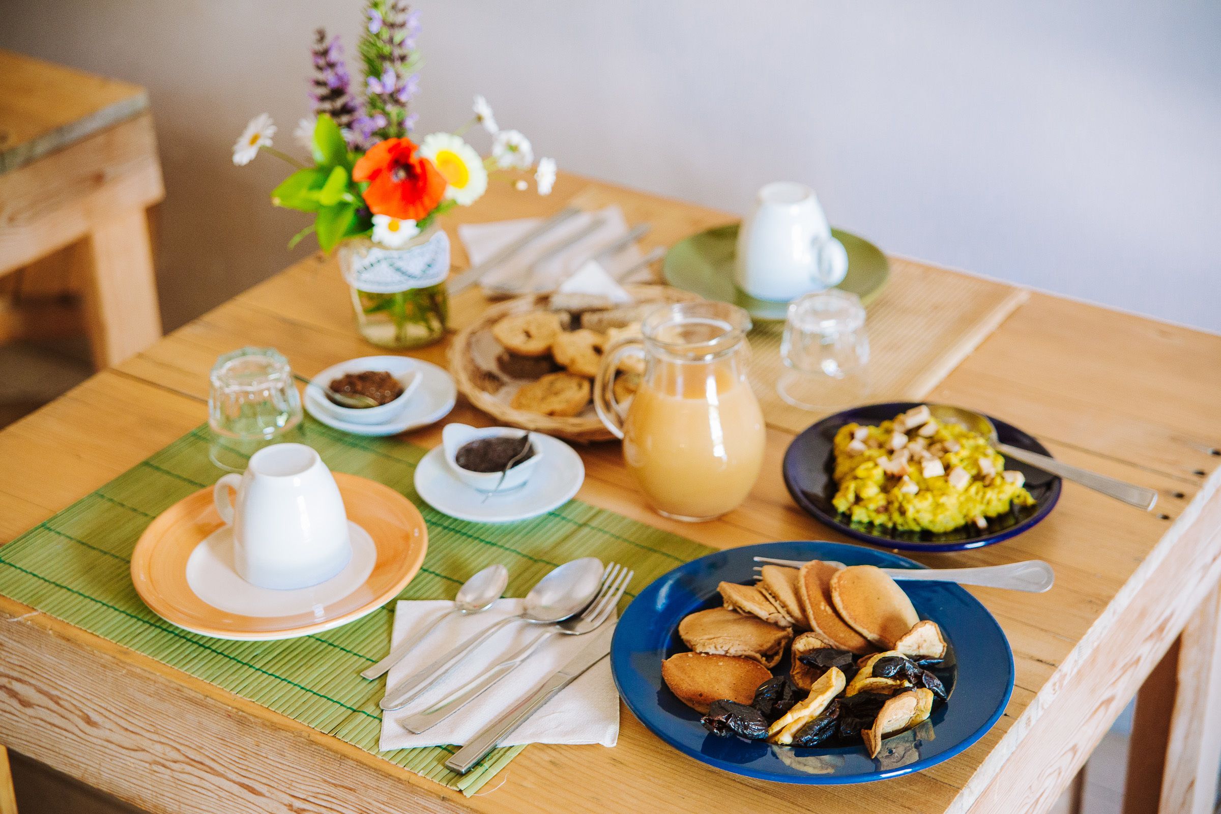 Una mesa de desayuno con diferentes platos, una jarrón y un florero con flores.