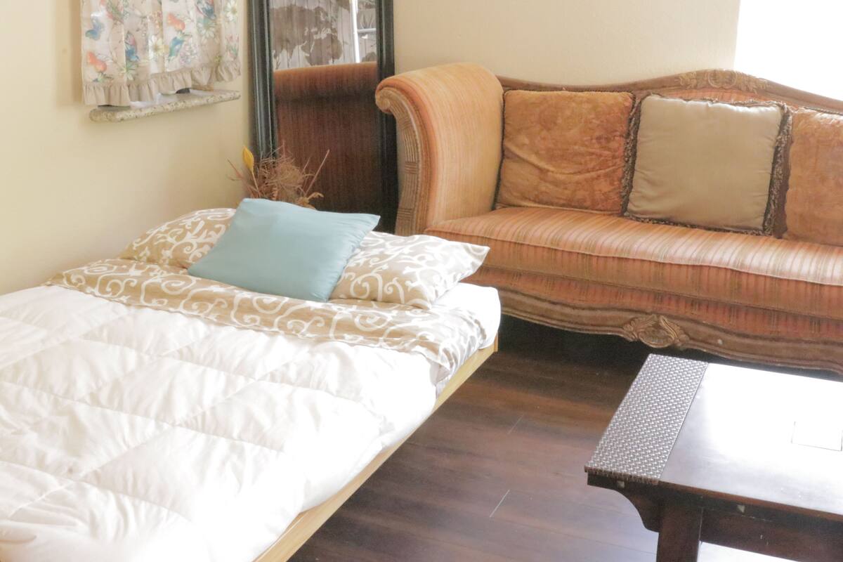Ein Schlafzimmer mit einem Bett, einem Holznachttisch, einem braunen Sofa und einem kleinen Tisch.