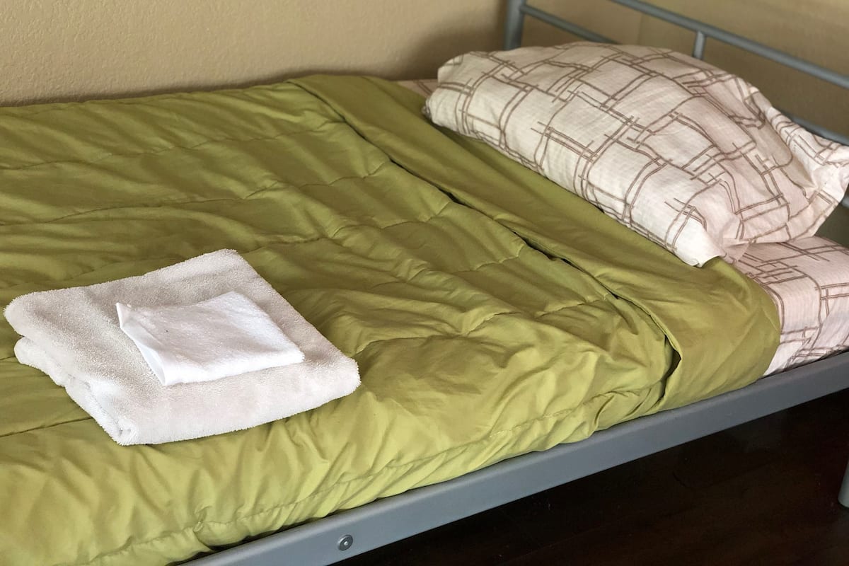 Ein Einzelbett mit einer grünen Decke, einem weißen Handtuch und zwei gemusterten Kissen.
