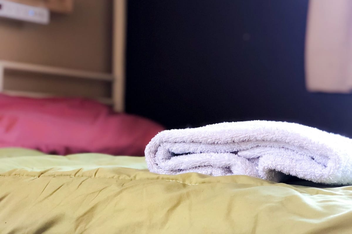 Ein ordentlich gefaltetes weißes Handtuch auf einer grünen Bettdecke in einem Hotelzimmer.