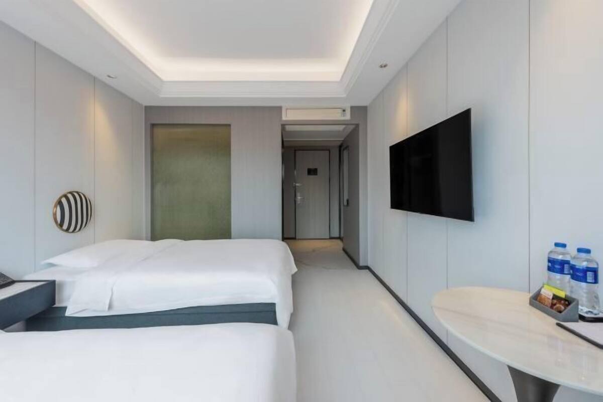 A hotel room with two beds, a flat-screen TV, a bedside table with water bottles, and a modern design.