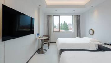 Habitación de hotel con dos camas, televisión montada en la pared, una mesita y una ventana con cortinas.