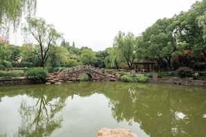 Un parc paisible avec un pont de pierre enjambant un étang, entouré d’une végétation luxuriante et agrémenté d’un belvédère.