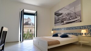 A bedroom with a bed, a nightstand, a lamp, and a large window with a view of a building and a boat. - Santi e Saraceni (Salerno)