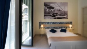 A bedroom with a bed, a window with curtains, a wall-mounted picture, and a bedside table with a lamp. - Santi e Saraceni (Salerno)