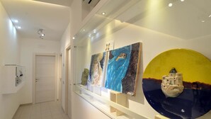 A hallway with a white door, a glass display case with art, and a yellow and blue decorative plate on the wall. - Santi e Saraceni (Salerno)