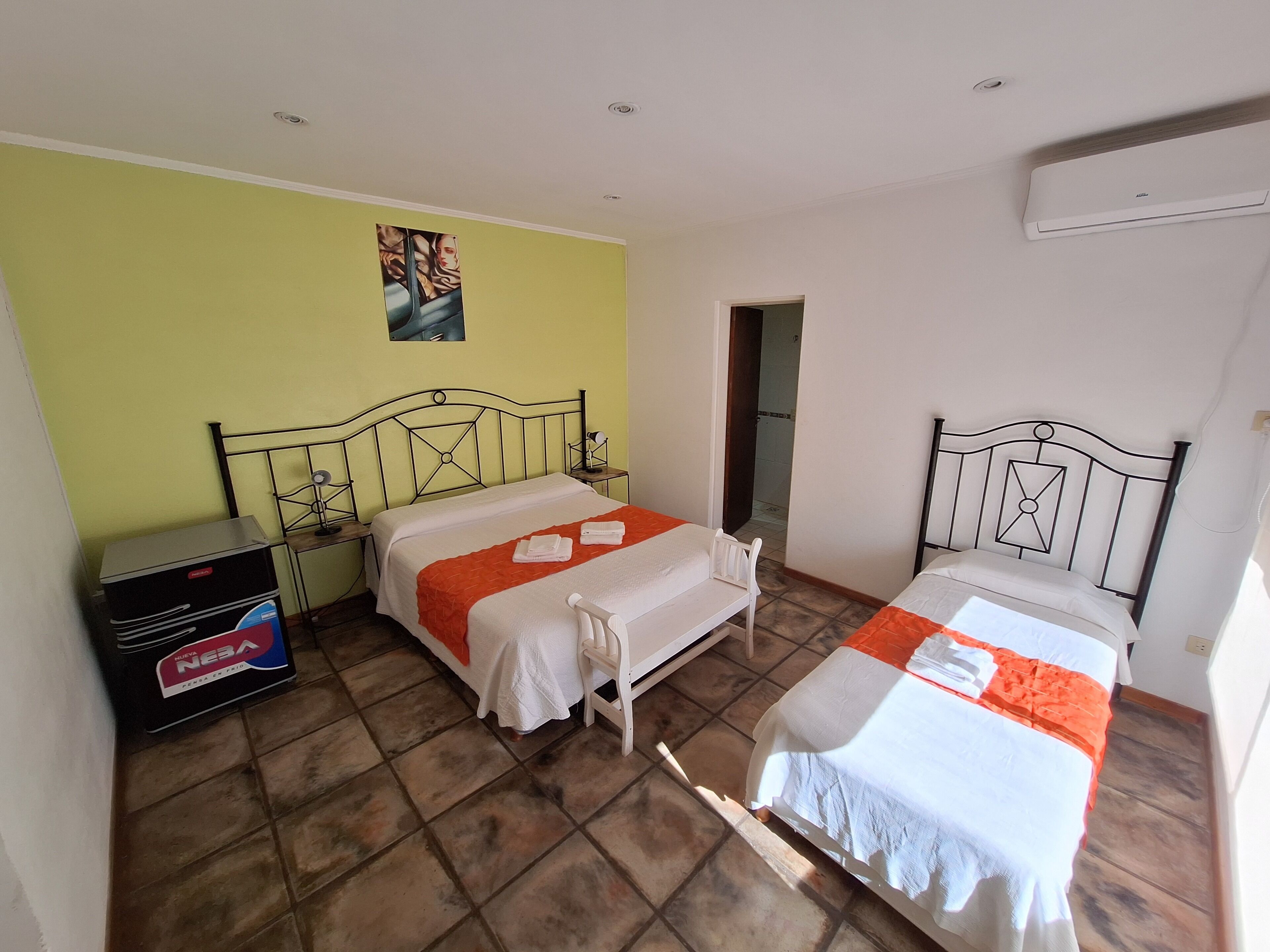 Quarto com duas camas, uma mesa de cabeceira, um aquecedor e um quadro na parede.