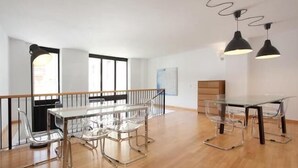 A modern office space with a glass table and chairs, black pendant lights, and a wooden railing. - Park Guell Apartments (Barcelona)