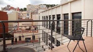 A balcony with a view of a cityscape, featuring a modern building with multiple windows and a chair. - Park Guell Apartments (Barcelona)