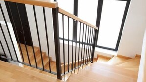 A wooden staircase with a black metal railing leading to a room with large windows. - Park Guell Apartments (Barcelona)