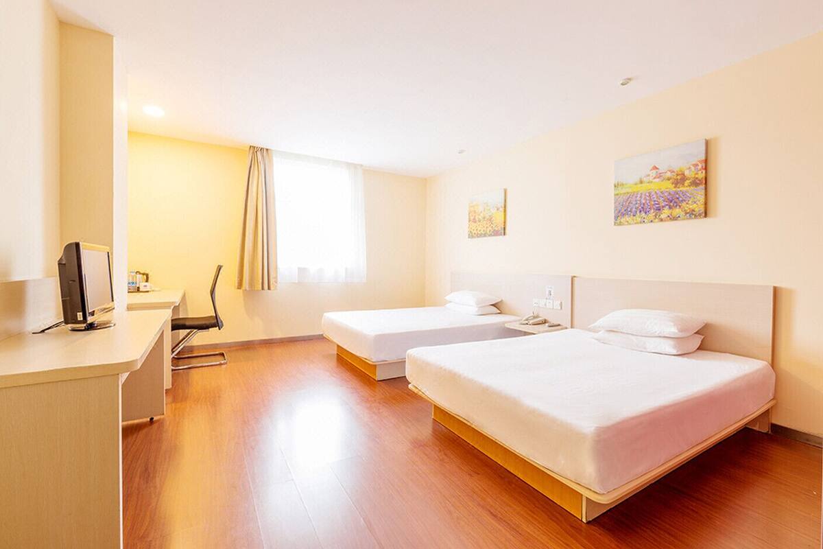 A hotel room with two beds, a desk with a computer, and a window with curtains.