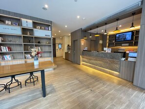 A modern reception area with a marble counter, wooden shelves with books, and a wooden floor. - Hanting Hotel (Shanghai)