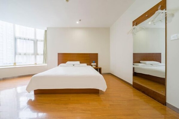 Camera d'albergo con un letto grande, una testiera in legno, uno specchio a figura intera e una finestra che lascia entrare luce naturale.
