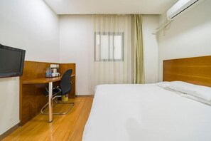 Una camera d'albergo con un letto, una scrivania con una sedia, un televisore e una finestra con tende.