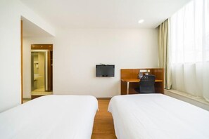 A hotel room with two single beds, a desk with a chair, a flat-screen TV, and a window with curtains.