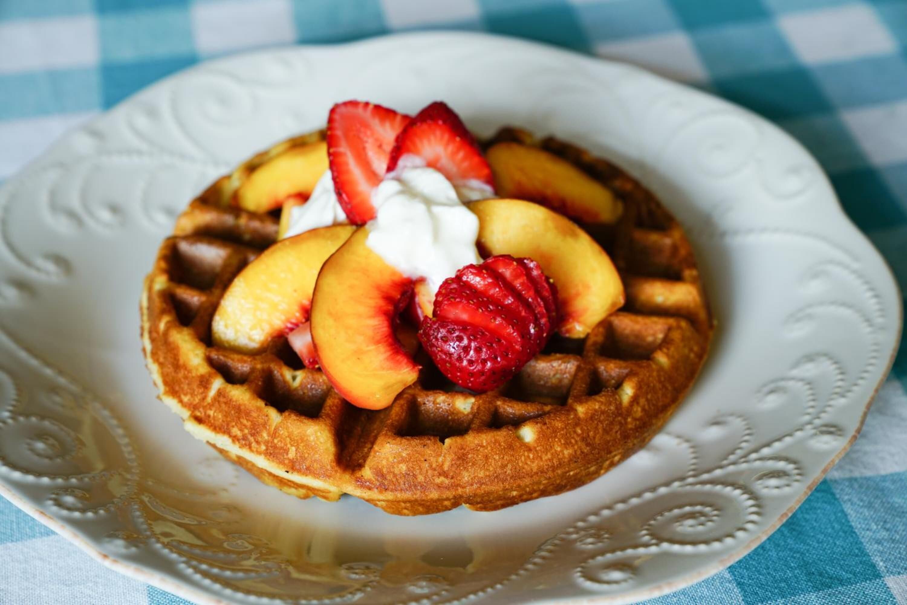 A waffle with sliced peaches and strawberries on a white plate.