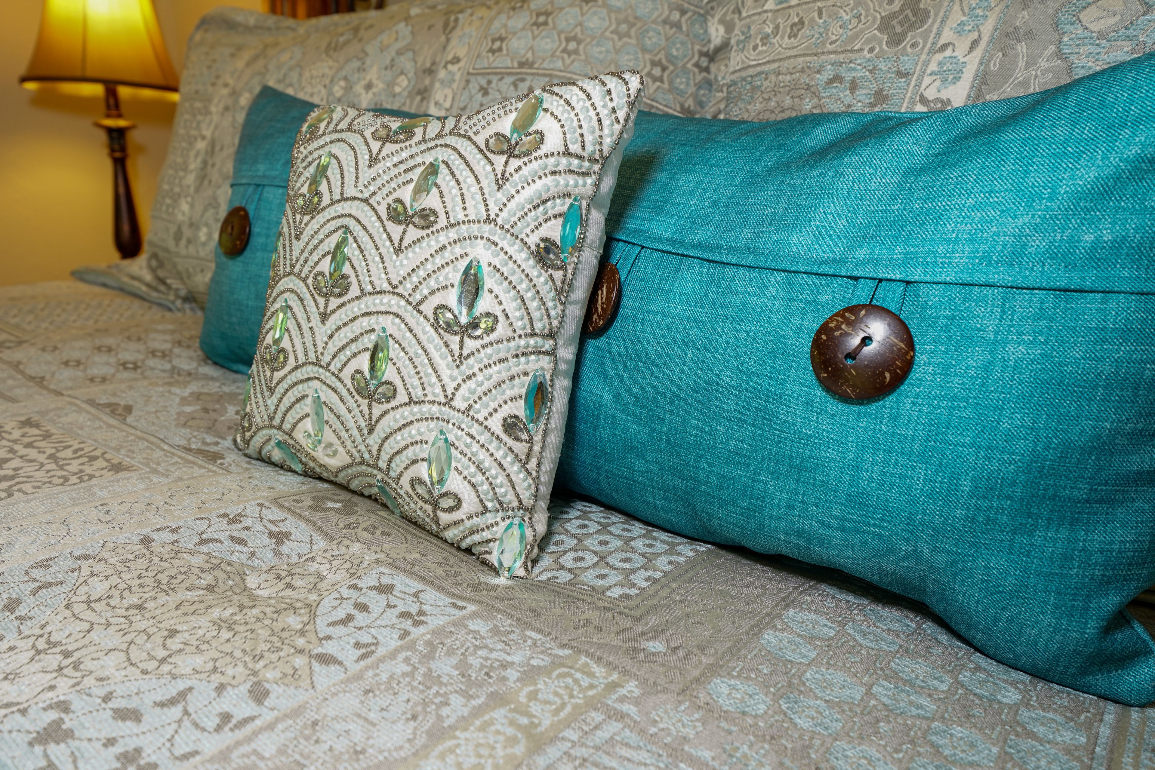 Een bed met beddengoed met een patroon en teal kussens met houten knopen.