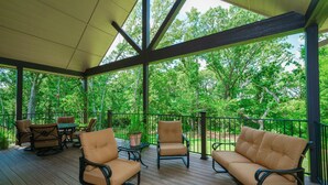 A covered outdoor deck with wooden flooring, cushioned chairs, and a table. - Hidden Meadows B&B (Stillwater)