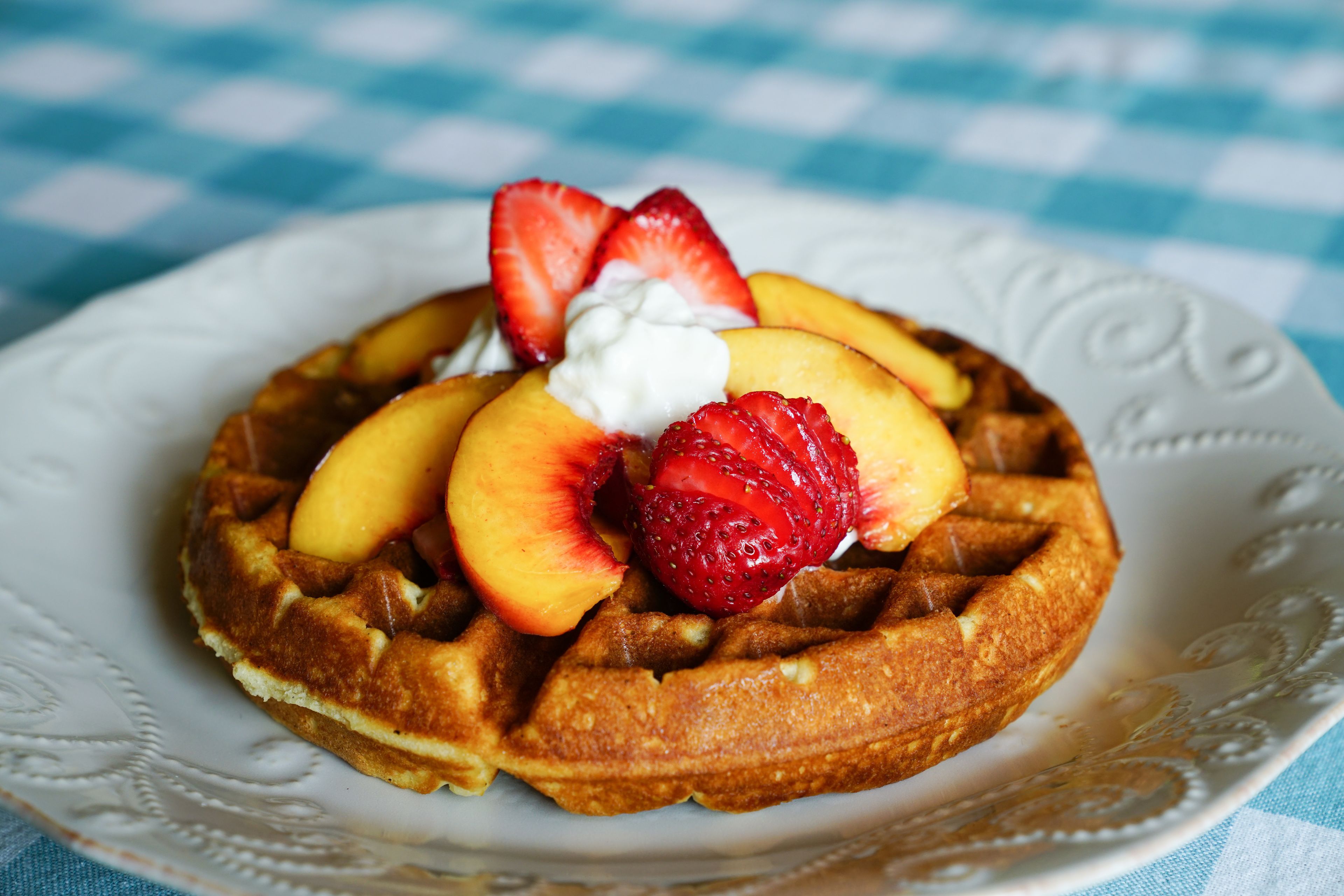 Um prato com um waffle coberto com pêssegos e morangos fatiados, e uma colherada de chantilly.