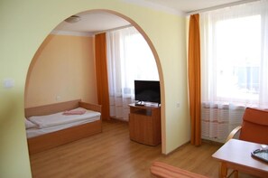 Ein gemütlicher Raum mit Bett, Fernseher, kleinem Tisch und einem Fenster mit Vorhängen.