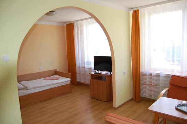 A compact room with a bed, a TV, a small table, and a window with curtains.