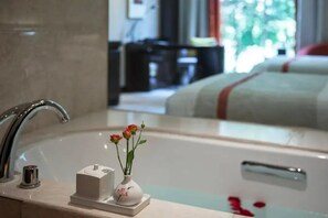 Une salle de bain dotée d’un lavabo moderne, d’un petit vase avec des fleurs et d’une baignoire parsemée de pétales de roses.