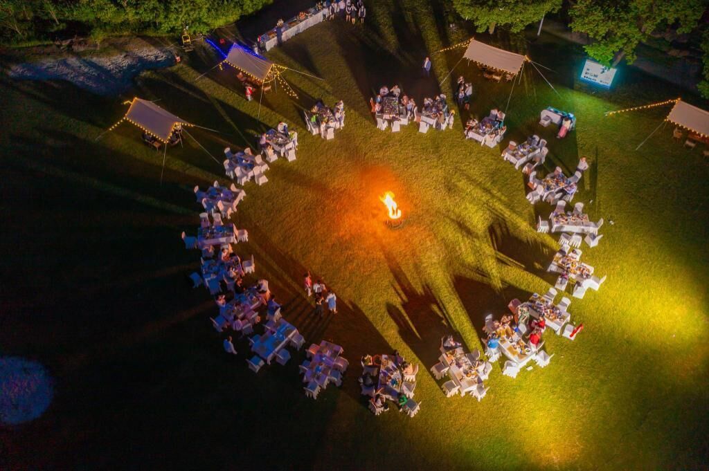 An aerial view of a circular gathering with tables and chairs arranged around a central fire.