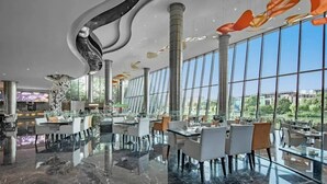 Ein modernes Restaurant mit einem Essbereich aus Glas, großen Fenstern und einem eleganten, geschwungenen Deckenbau.