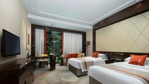 Ein Hotelzimmer mit zwei Betten, einem Fernseher, einem Schreibtisch und einem Fenster mit Vorhängen.