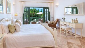 A spacious bedroom with a large bed, a sitting area with a chair and table, a vanity with a mirror, and a view of greenery through the door. - The Summer House, Sugar Hill Resort (Holetown)