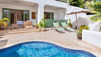 Zona de piscina con sillones reclinables y plantas en macetas.