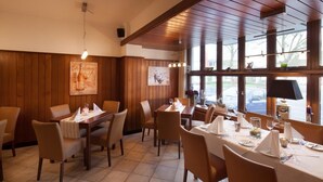 Um restaurante com paredes de painel de madeira, grandes janelas e mesas preparadas para refeições.