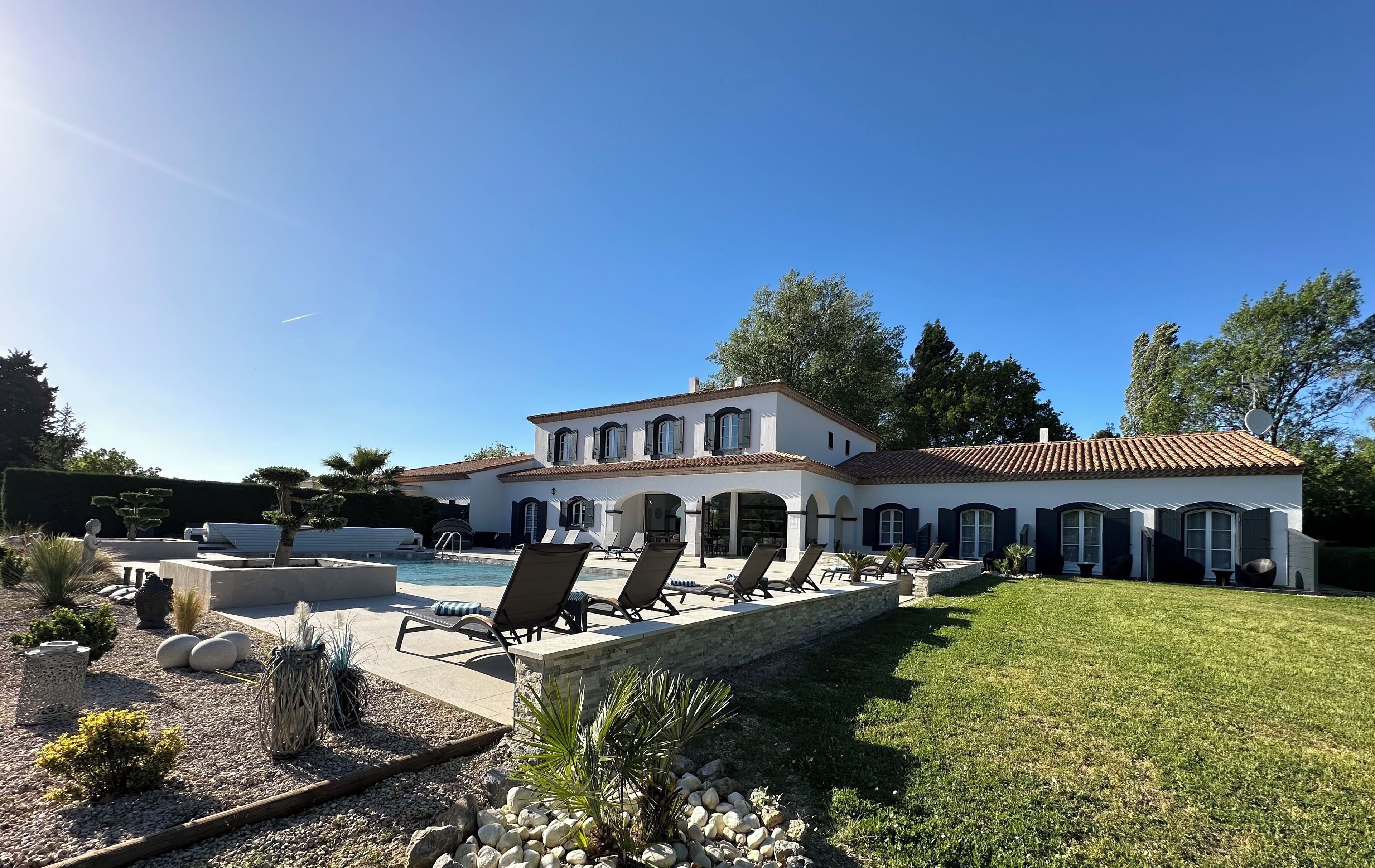 A large white house with a tiled roof, a swimming pool, and outdoor seating.