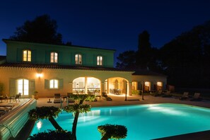 Una casa de dos pisos con piscina, mobiliario de exterior y un patio bien iluminado.