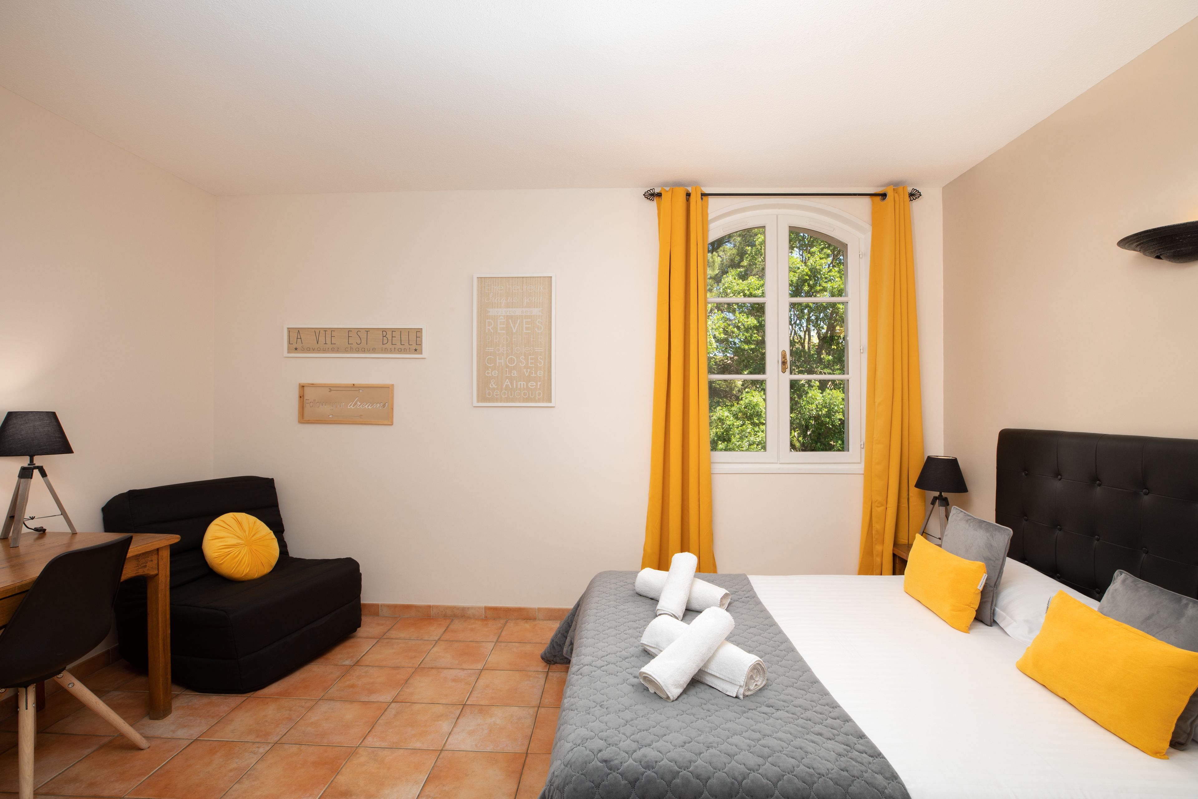 Une chambre d’hôtel avec un lit, un bureau, une chaise et une fenêtre avec des rideaux.