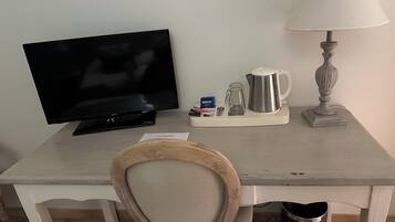 Una habitación pequeña y sencilla con televisión, lámpara, cafetera y cubo de basura.