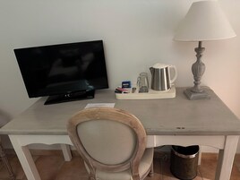 Una habitación pequeña y sencilla con televisión, lámpara, cafetera y cubo de basura.