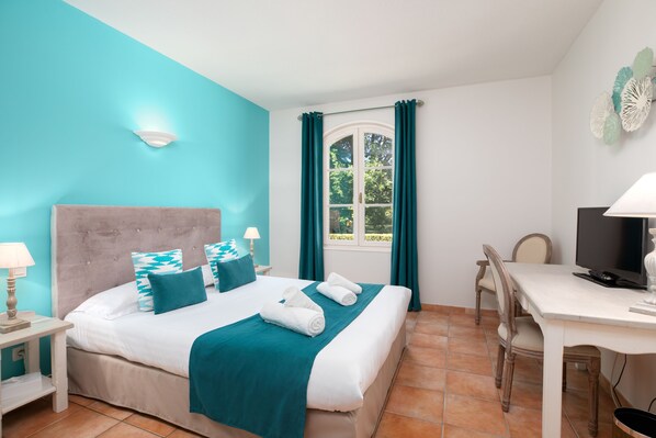 Un dormitorio con cama, escritorio, silla, televisor y ventana con cortinas.