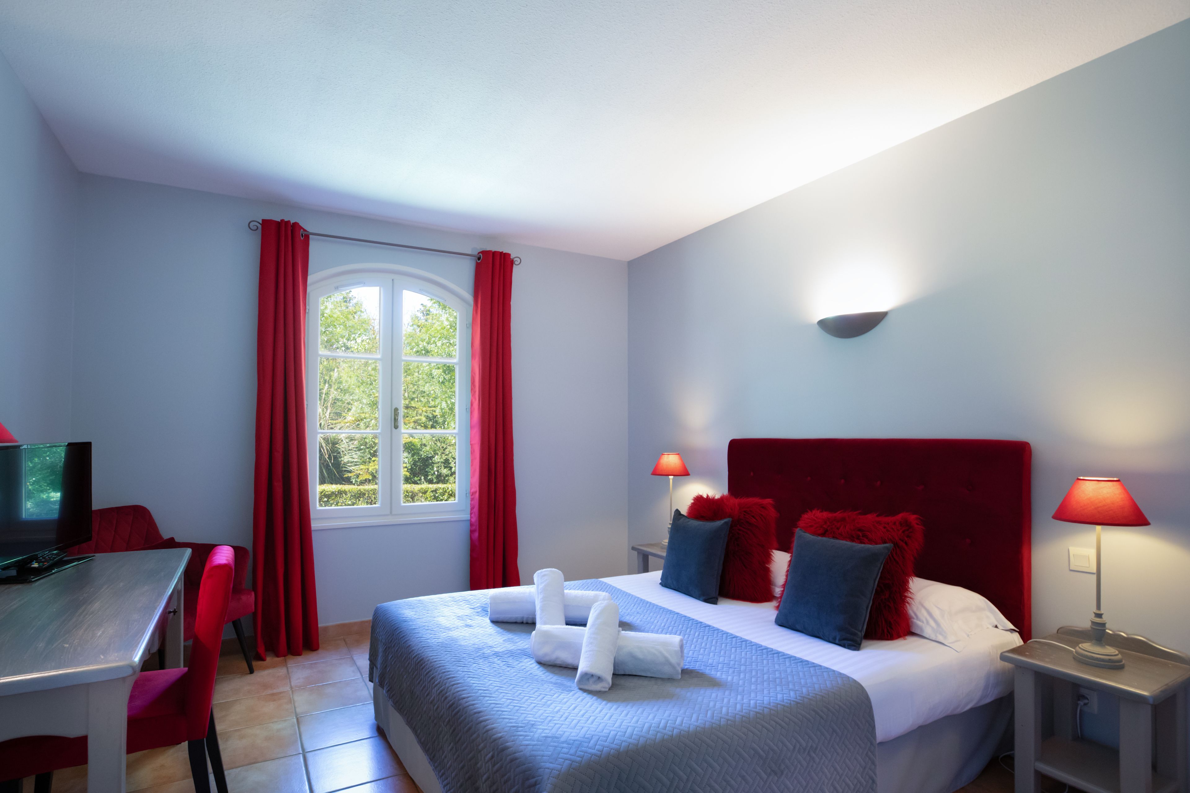 Habitación de hotel con cama, escritorio y ventana con cortinas rojas.