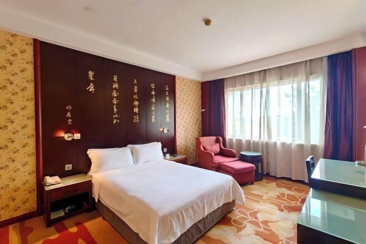 A hotel room with a bed, a desk, a chair, and a small table.