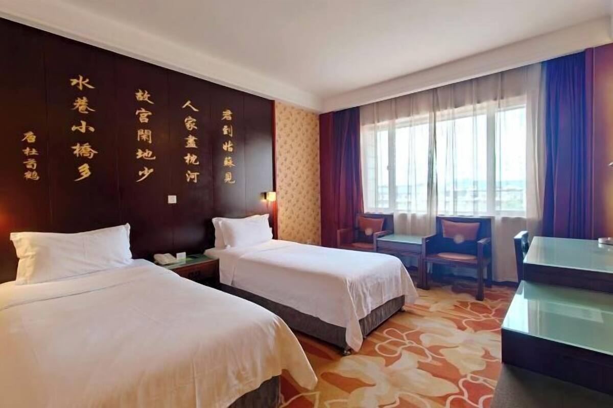 A hotel room with two beds, a desk, and a view of the city.